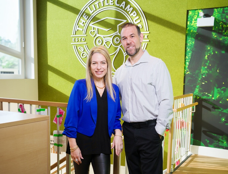 Tami and Carl standing by a staircase in front of a The Little Campus logo